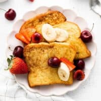 Three pieces of brioche french toast plated with banana slices and fresh berries