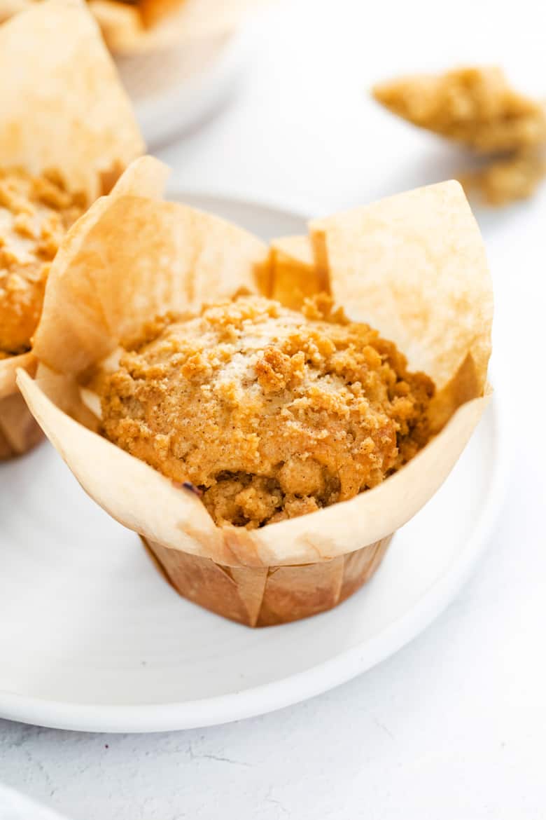 Crumb cake muffin in brown wrapper on a white plate