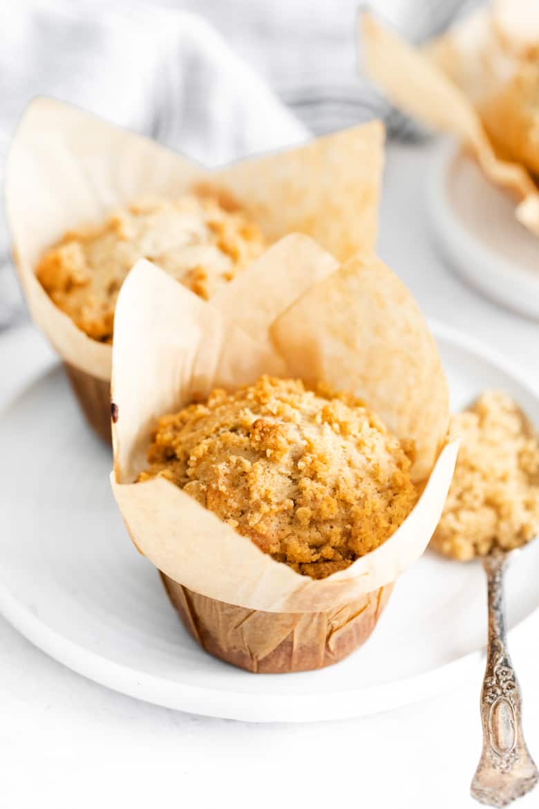 Golden coffee cake muffin topped with streusel; antoher cupcake is behind it and next to it is a spoonful of streusel