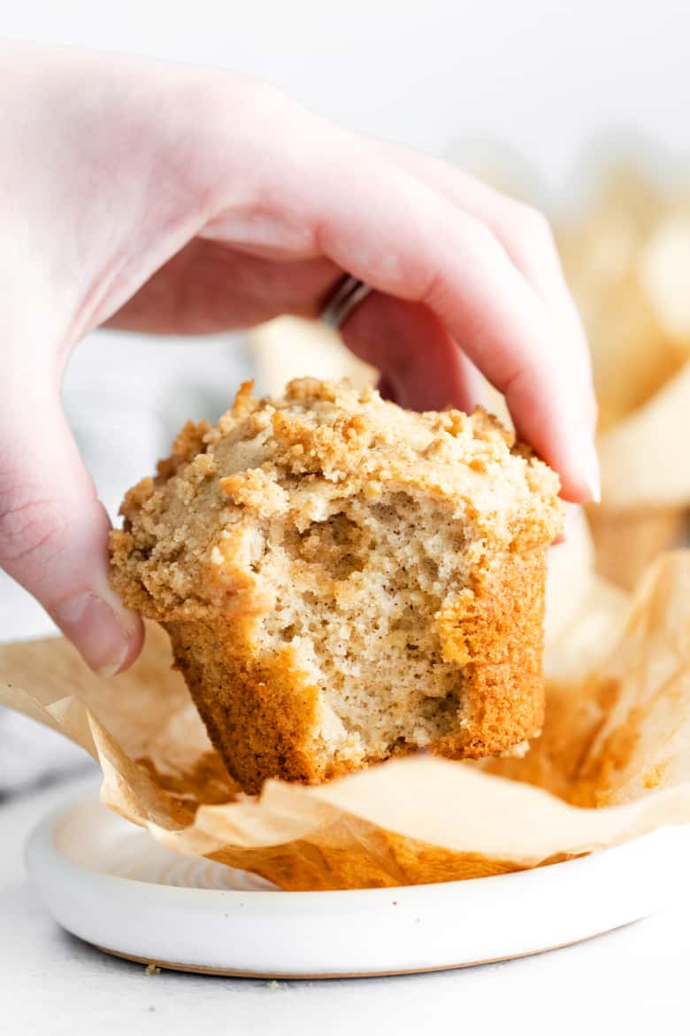 Hand holding coffee cake muffin with bite taken out of it to show soft cinnamon vanilla cupcake