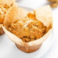 Crumb cake muffin in brown wrapper on a white plate