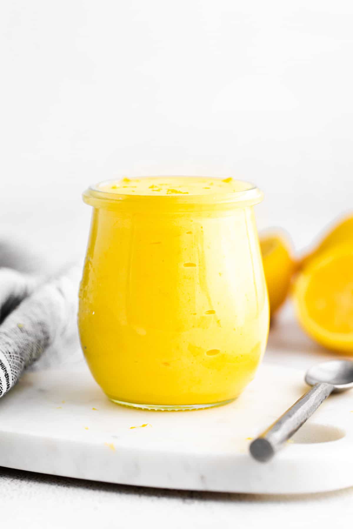 jar of homemade lemon curd with fresh lemons in background