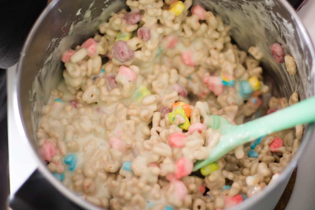 Lucky charms cereal being stirred into melted marshmallows in a large pot