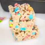 Three lucky charms marshmallow cereal bars cut into squares and stacked on top of one another on a white plate