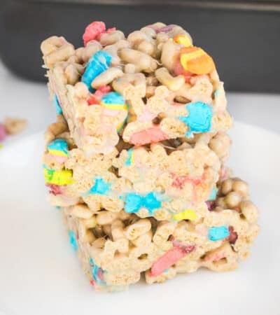 Three lucky charms marshmallow cereal bars cut into squares and stacked on top of one another on a white plate