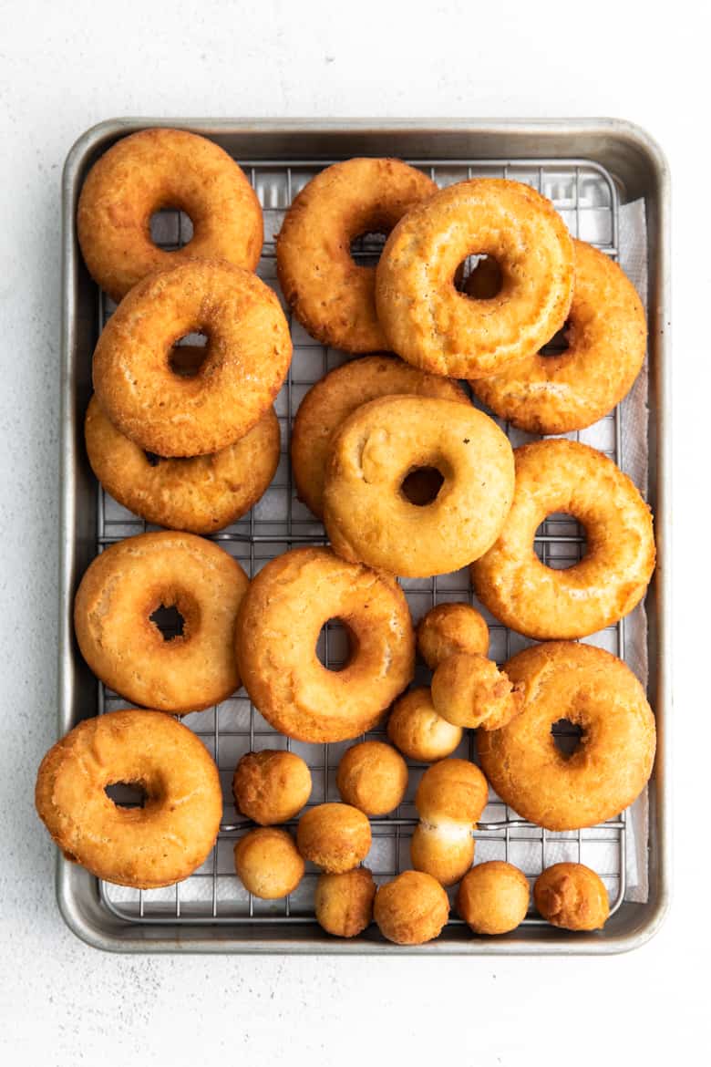 Golden brown freshly fried doughnuts on metal cooling rack over sheet pan