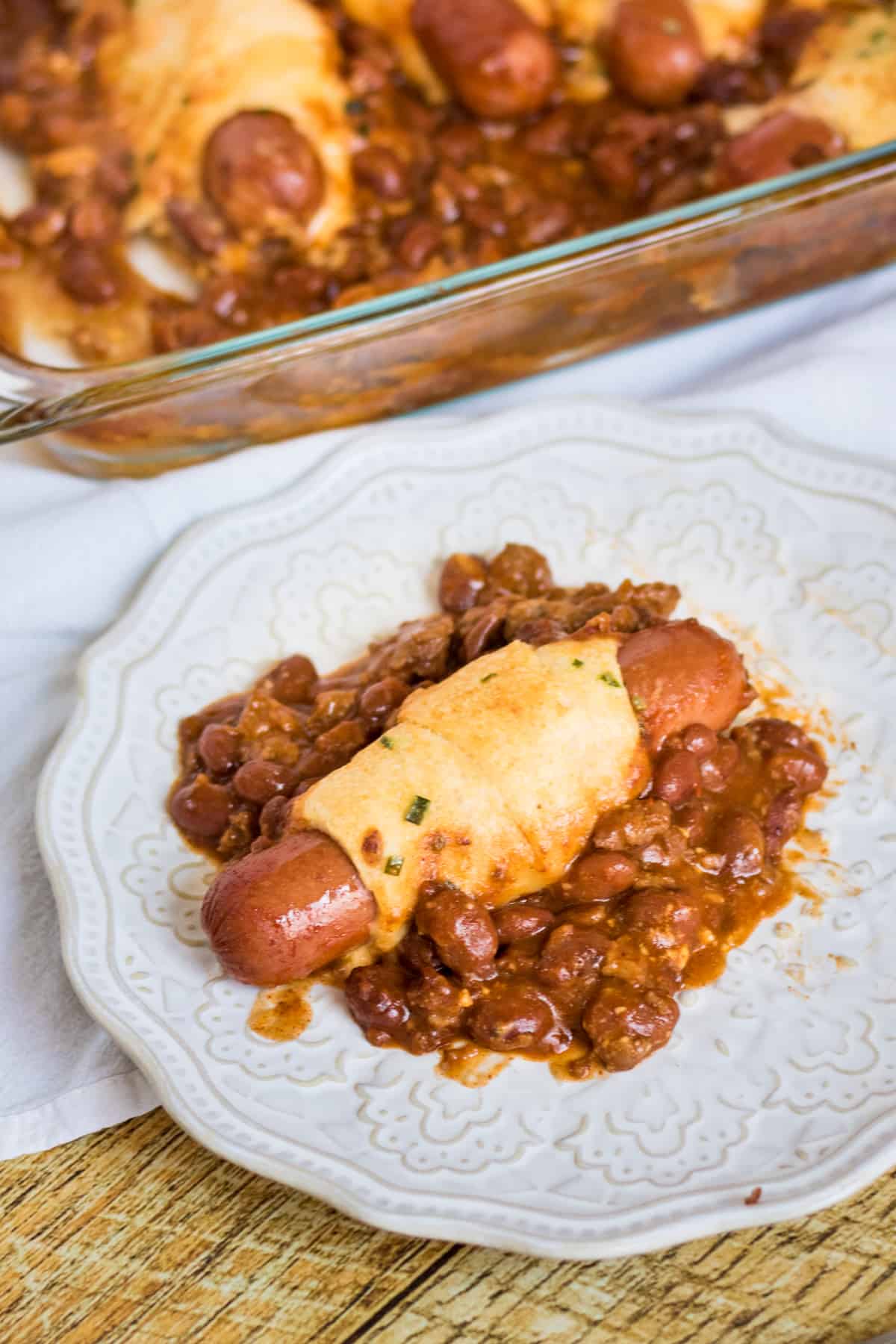 one chili cheese crescent hot dog on plate with casserole in background