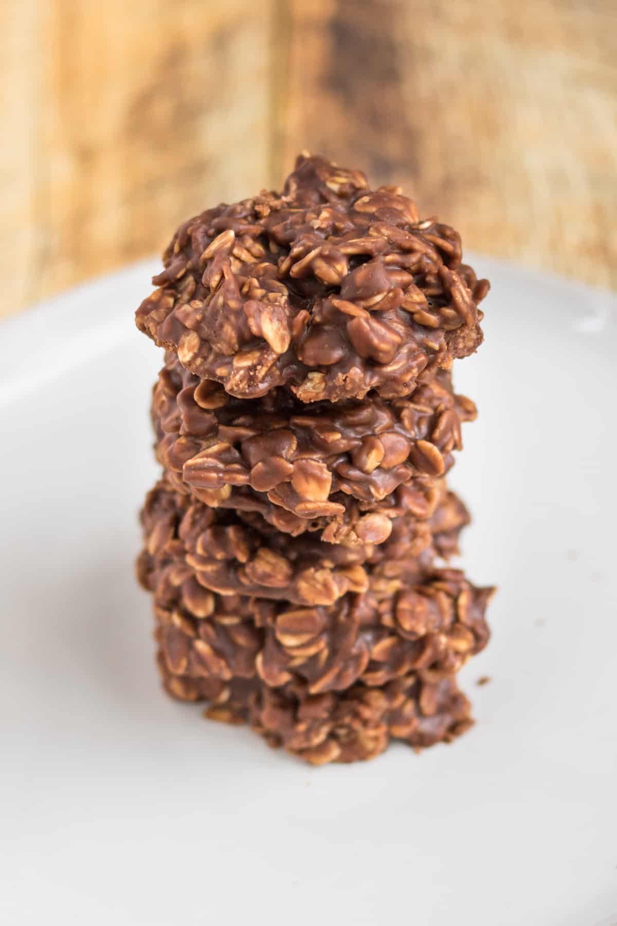 Five thick chocolate oatmeal cookies stacked one on top of another on a white plate.