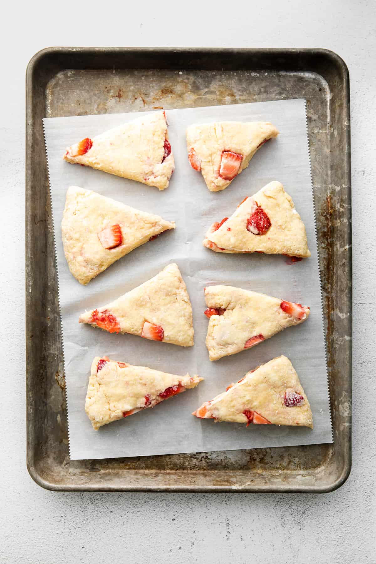eight unbaked strawberry scones cut into triangles and placed on a parchment-lined baking sheet