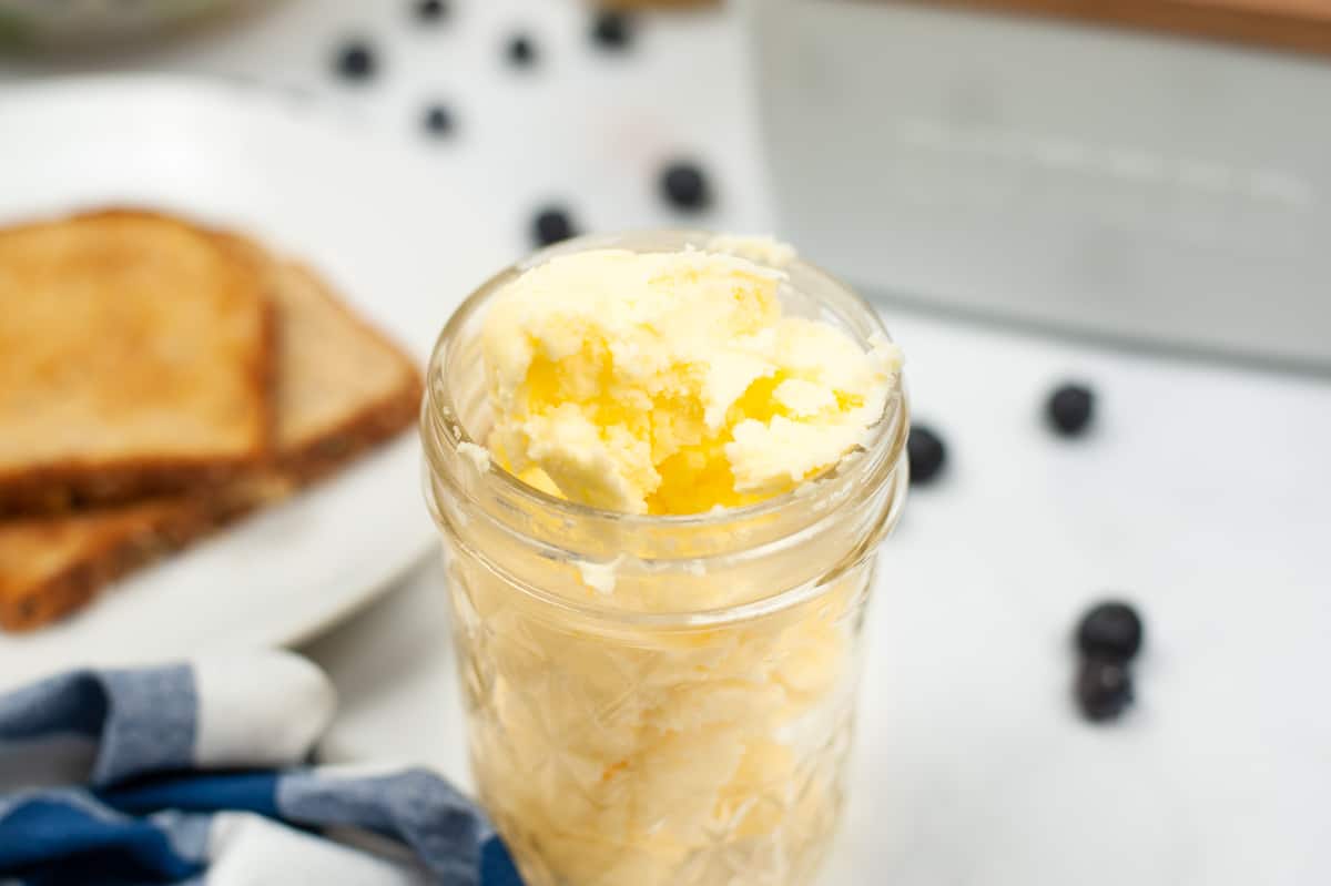 Jar of butter with toast and berries in background