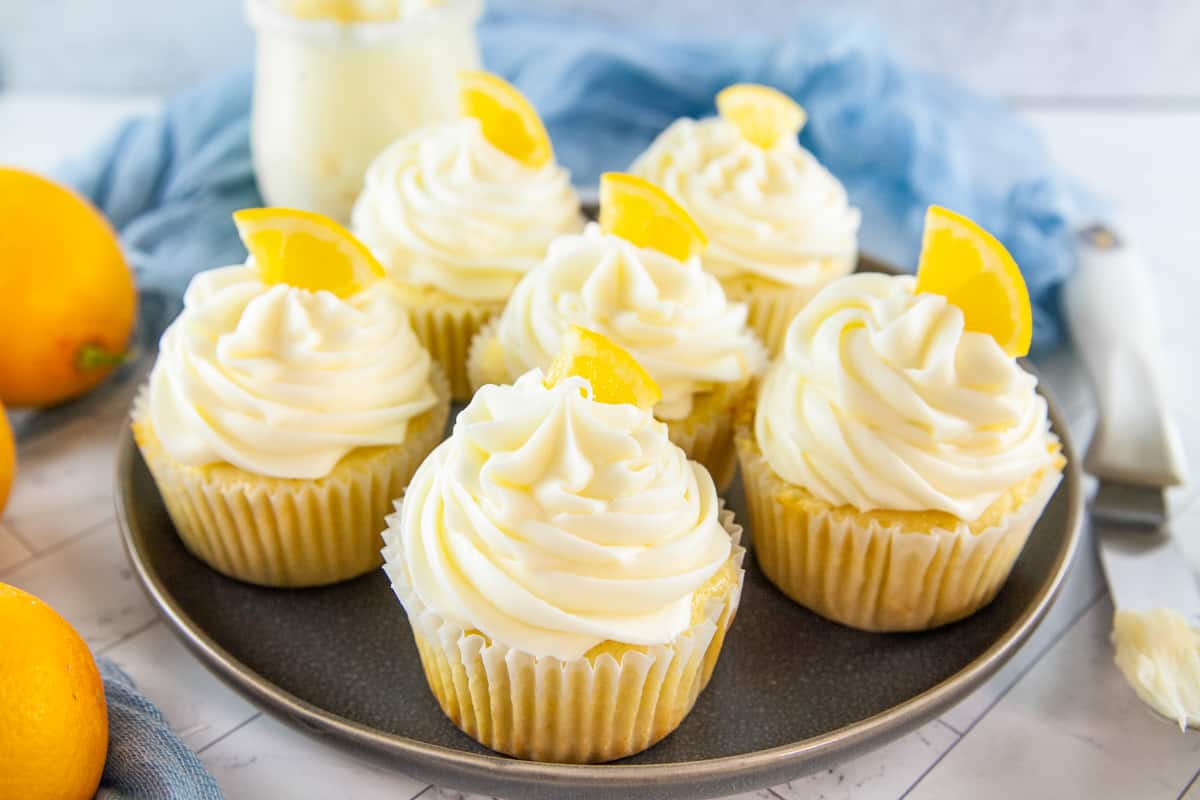 6 lemon cupcakes topped with icing and candied lemon wedges.