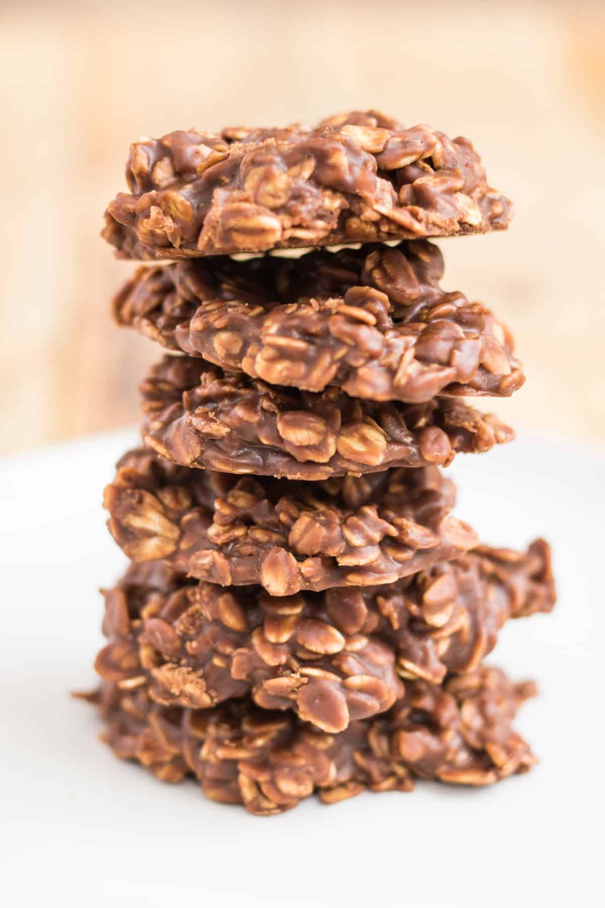 Side-view of 6 thick chocolate oatmeal cookies stacked one on top of another on a white plate.