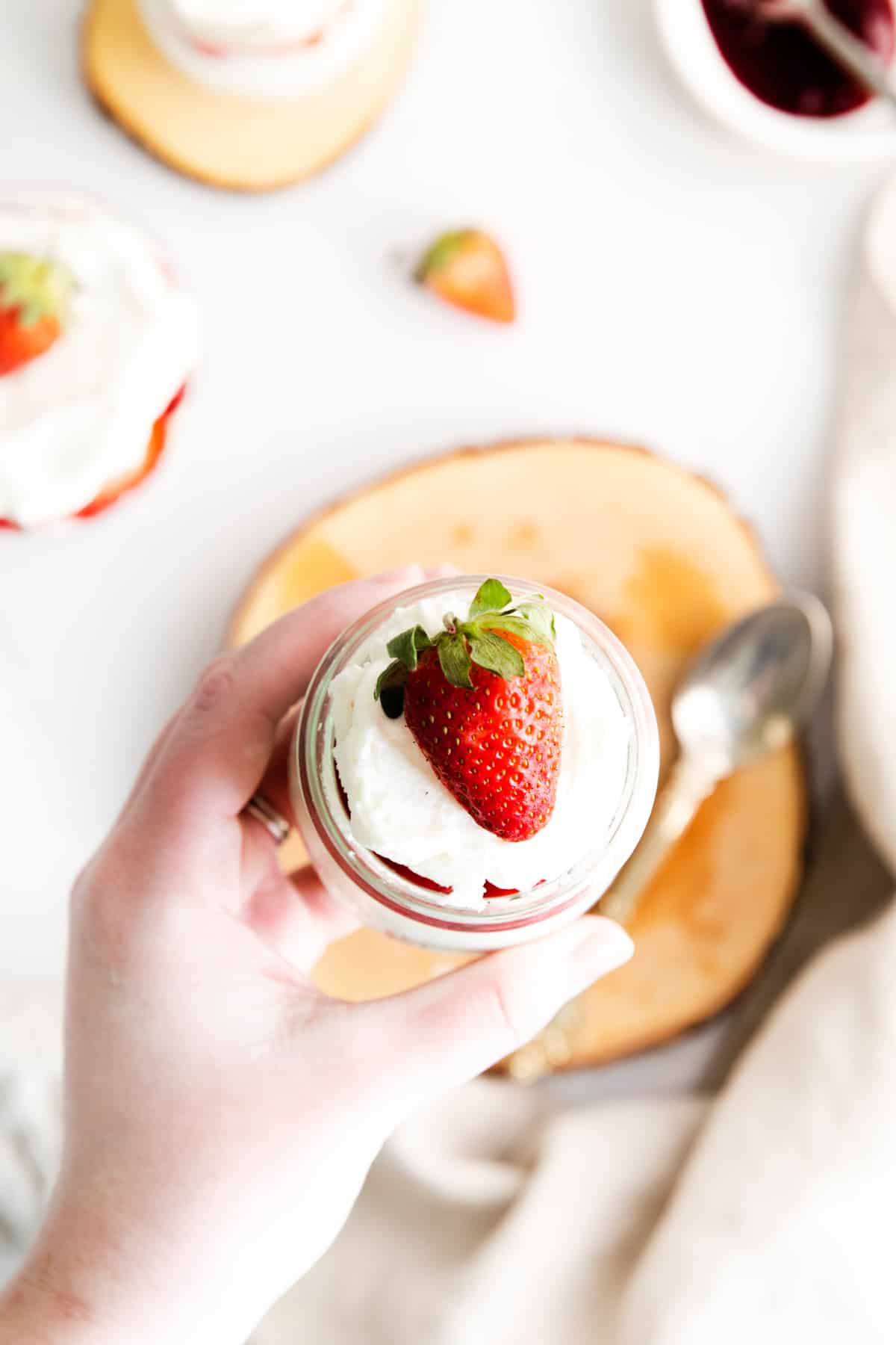 woman's hand holding small dessert cup topped with whipped cream and strawberry