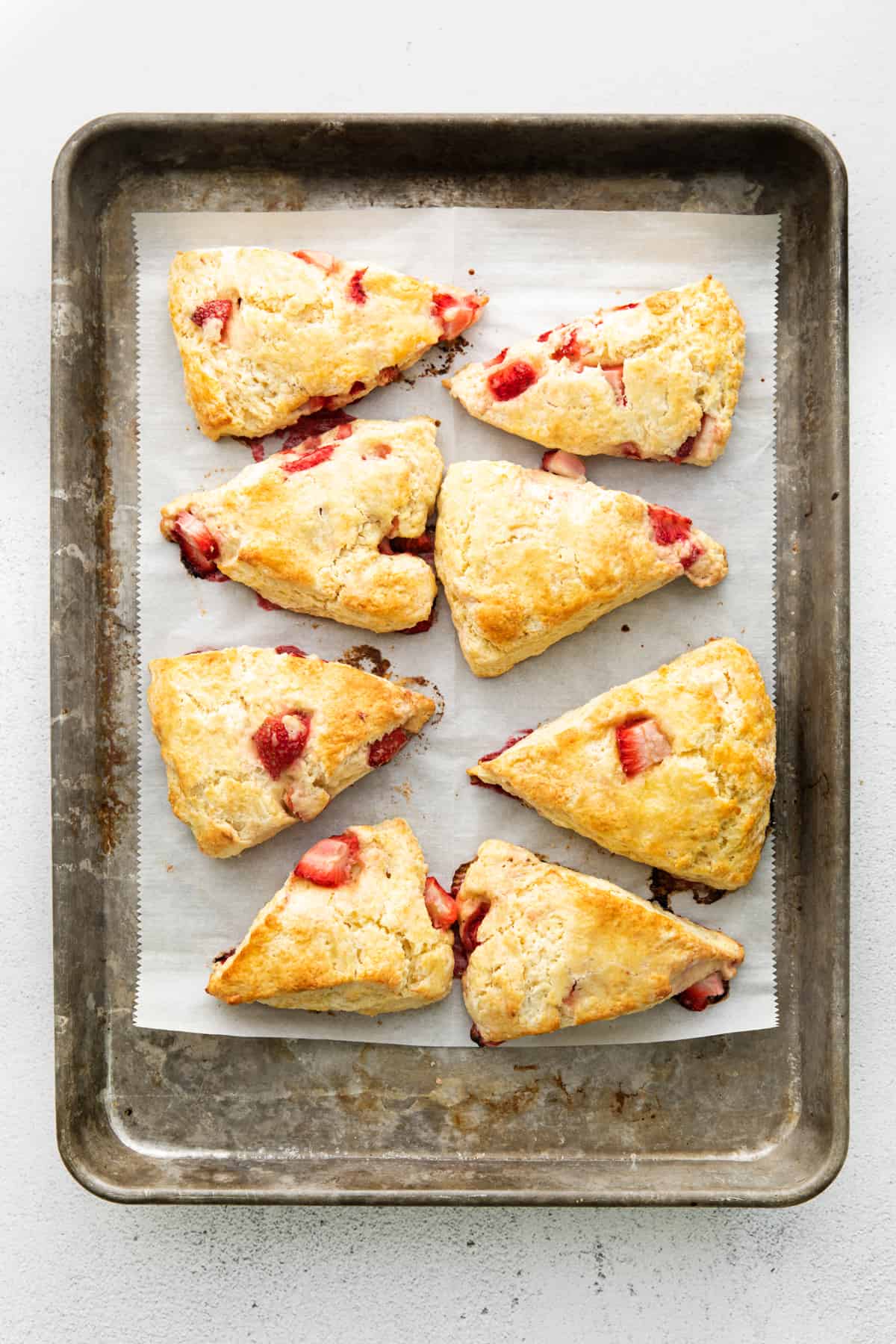 Eight golden brown strawberry scones on parchment-lined baking sheet