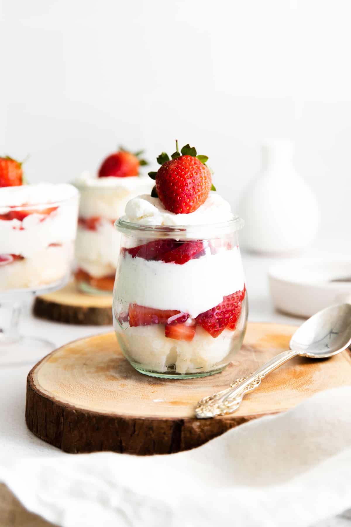 mini strawberry shortcake trifles in glass jars, showing their layers of angel food cake, fresh strawberries, and whipped cream