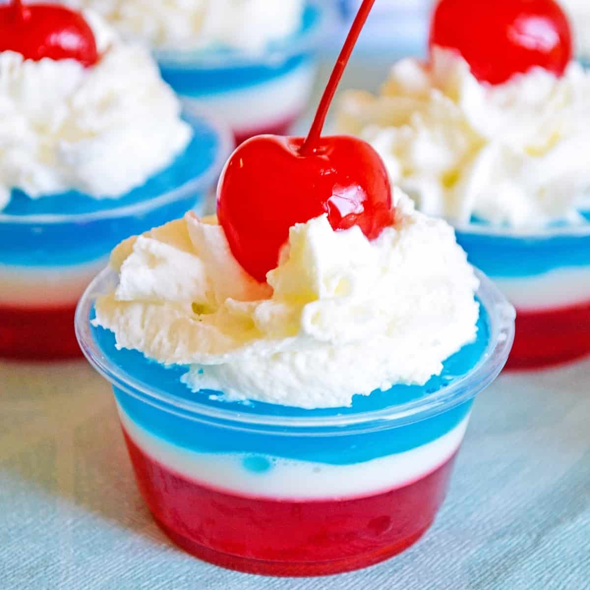 red, white, and blue layered jello shot topped with whipped cream and maraschino cherry