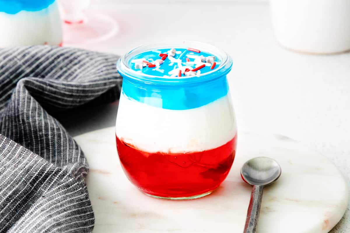 Patriotic jello and cool whip dessert cup in small glass with spoon next to it