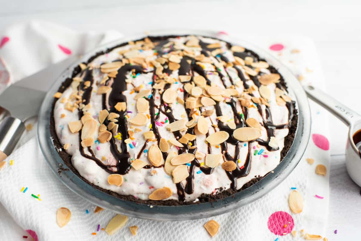Pie topped with ice cream sundae toppings: sprinkles, chocolate sauce, and sliced almonds