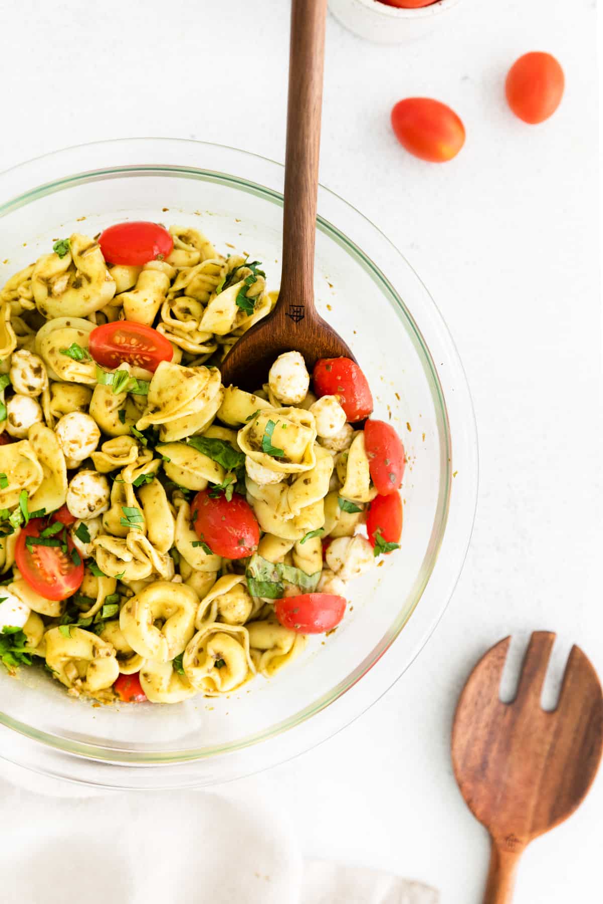 Wooden serving spoon in a bowl of tortellini pasta salad with pesto dressing