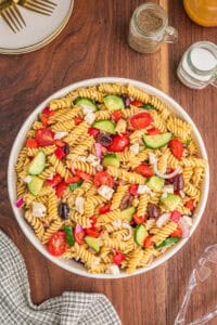 A bowl of with Greek pasta salad with rotini pasta, cherry tomatoes, cucumber slices, kalamata olives, feta cheese, red onion, and red bell pepper.