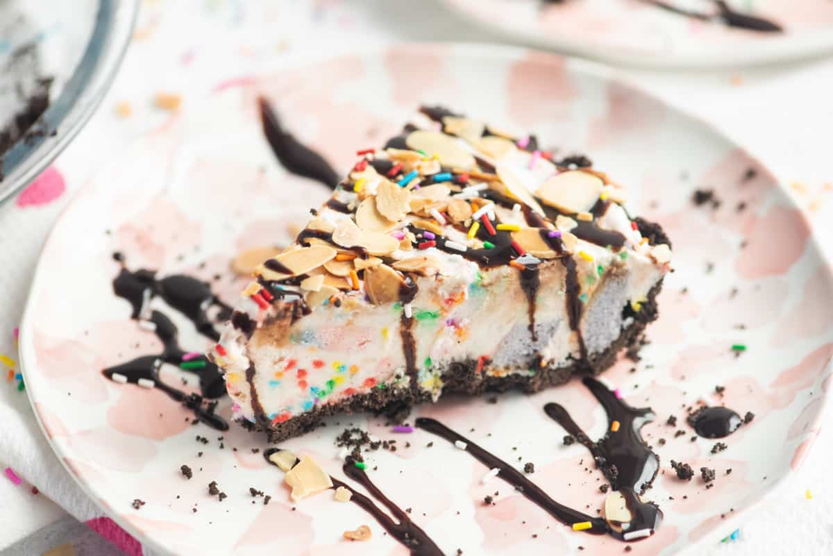 Slice of ice cream pie drizzled with chocolate sauce and topped with sprinkles and sliced almonds