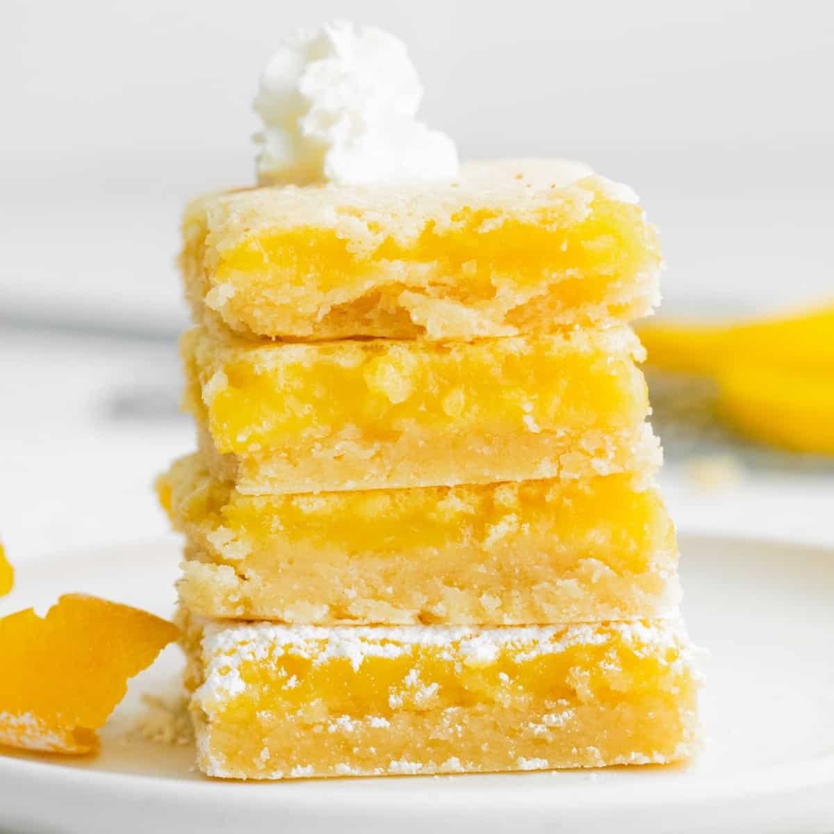 four lemon bars stacked on a white plate and topped with a dollop of whipped cream