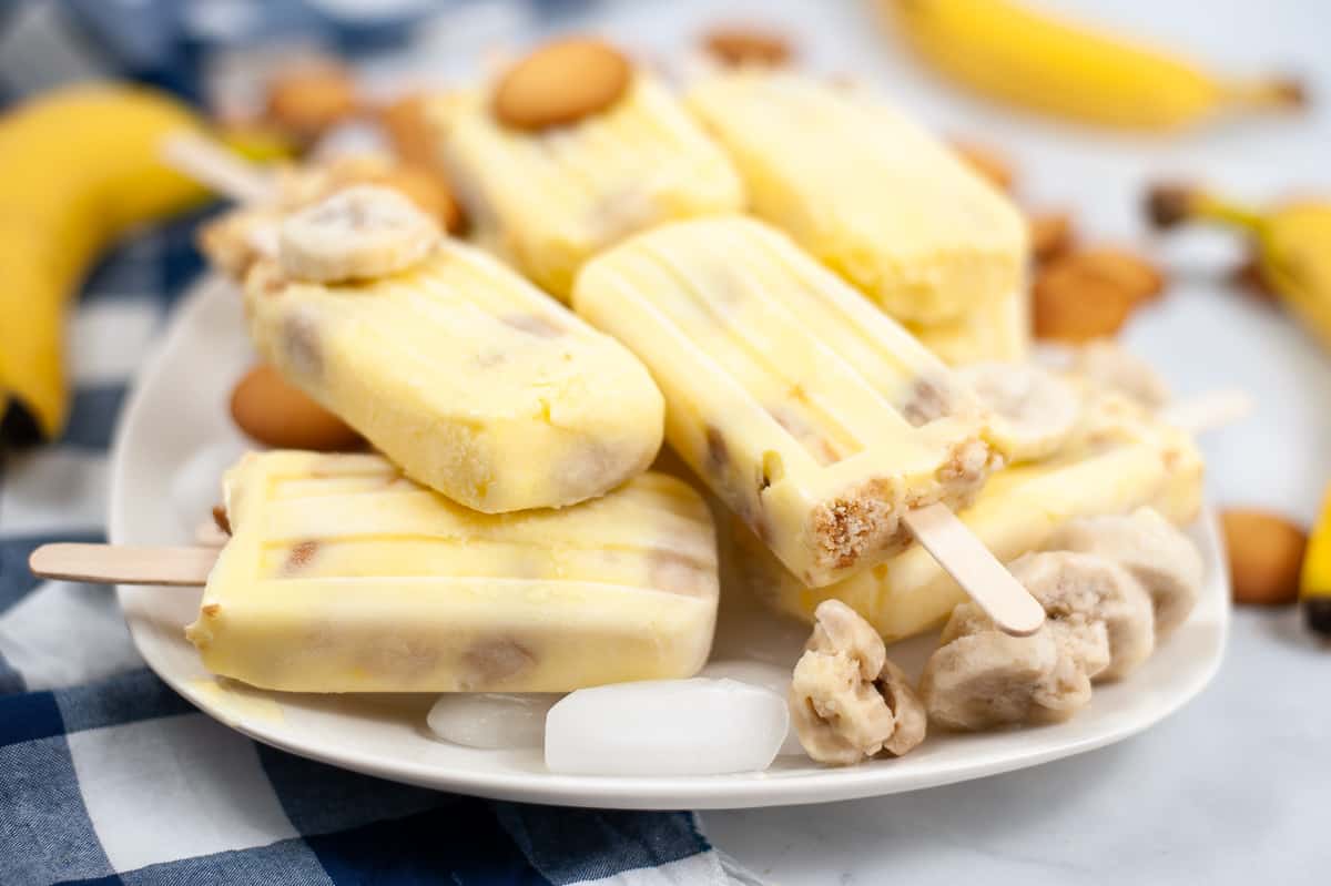 Banana pudding popsicles on a plate with vanilla wafers and frozen banana slices