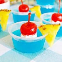 Bright blue jello shots garnished with whipped cream, cherries, and pineapple wedges