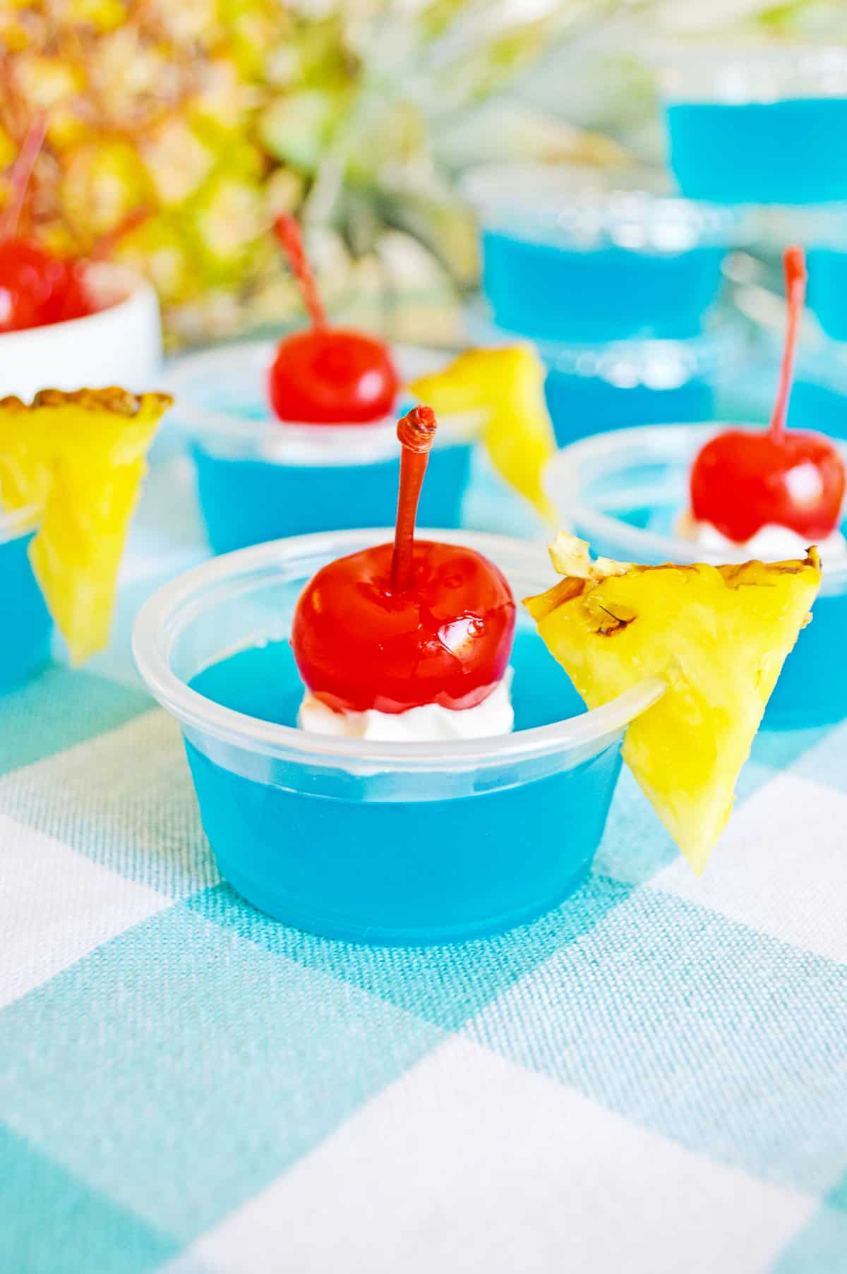 Blue Hawaiian Jello Shots in 2 oz plastic cups and garnished with whipped cream, cherries, and pineapple wedges