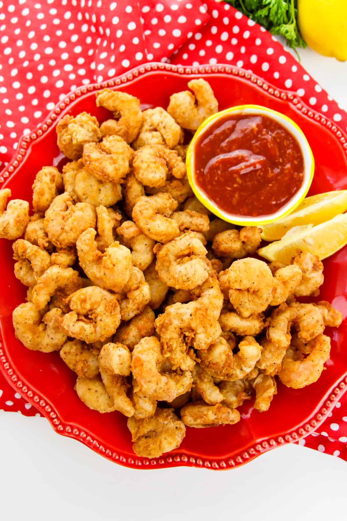 Popcorn shrimp with cocktail sauce and lemon wedges on red plate