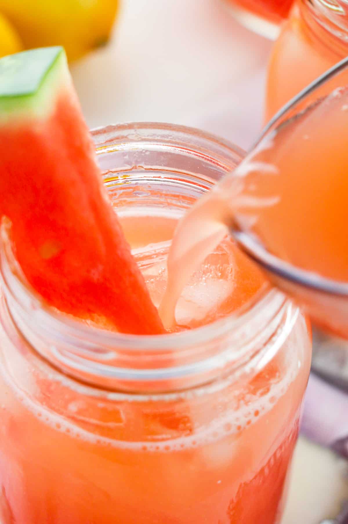 Watermelon lemonade being poured from pitcher into glass garnished with fresh watermelon
