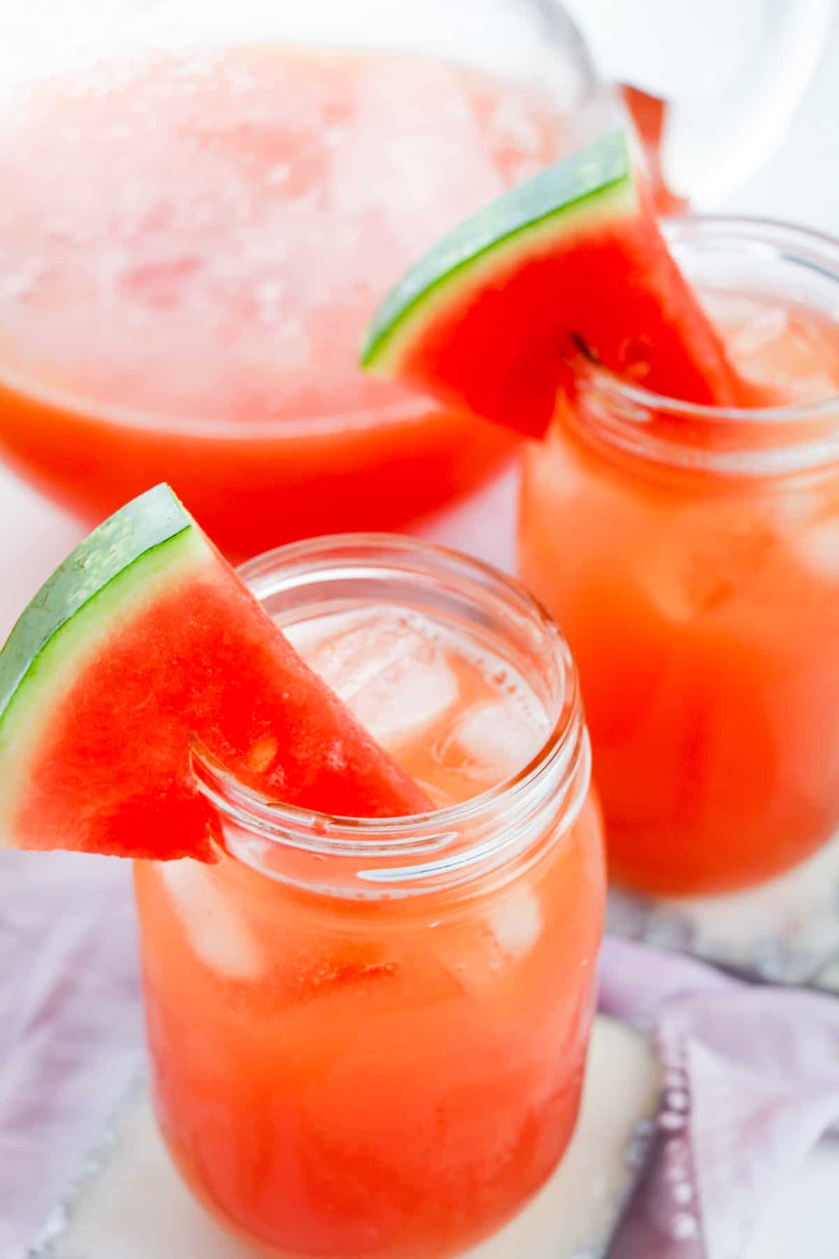Watermelon lemonade in glass pitcher and served in two glasses with fresh watermelon wedges for garnish