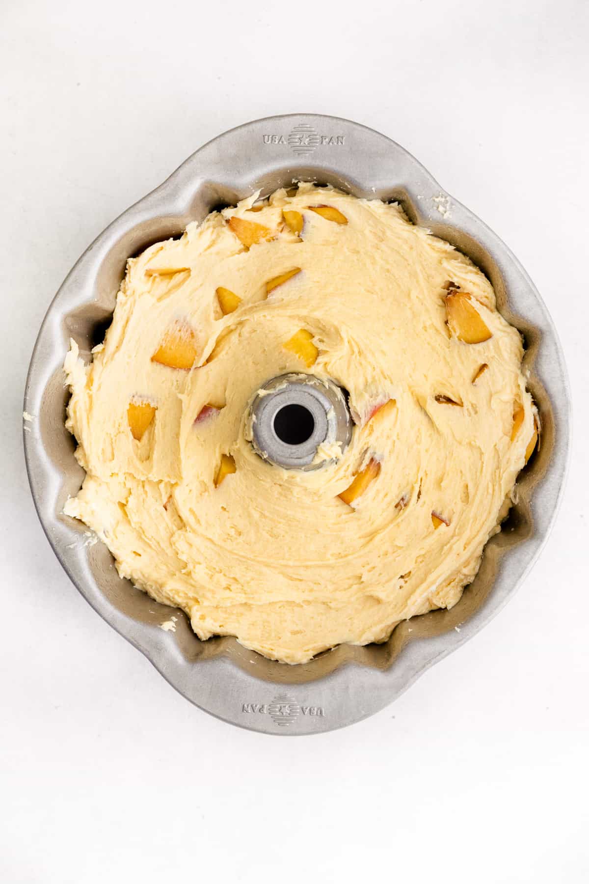 Bundt cake pan filled with batter with chunks of fresh peaches in it
