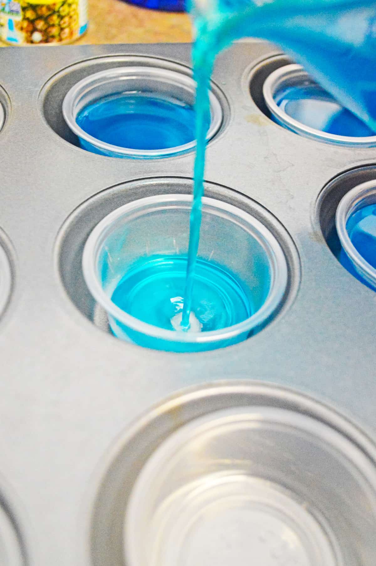 pouring blue liquid into small plastic shot glass in cavity of muffin tin