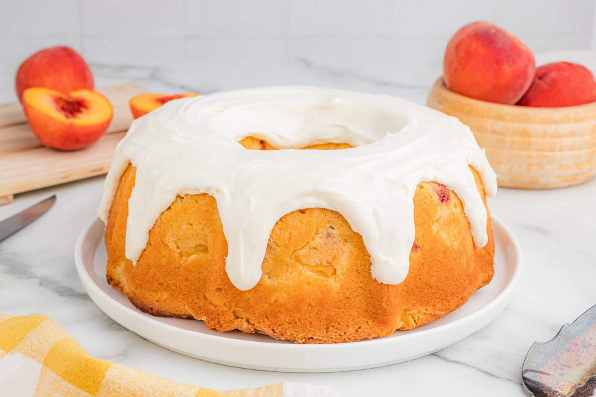 Whole peach bundt cake with cream cheese icing on a plate.