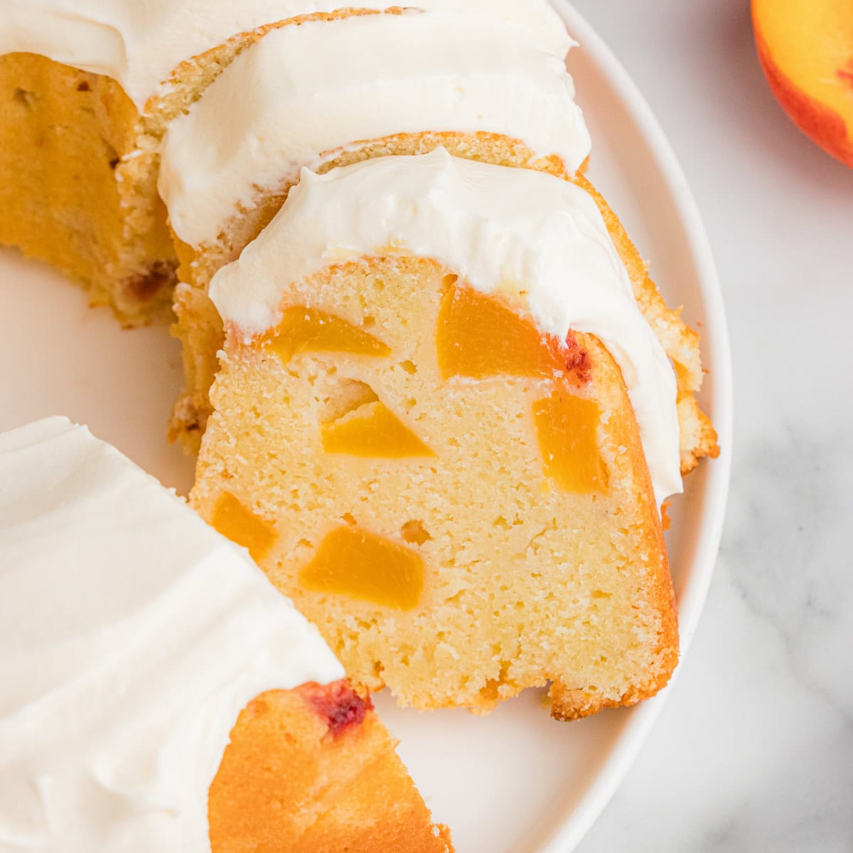 A sliced peach pound cake with cream cheese frosting and multiple chunks of fresh peaches distributed throughout.