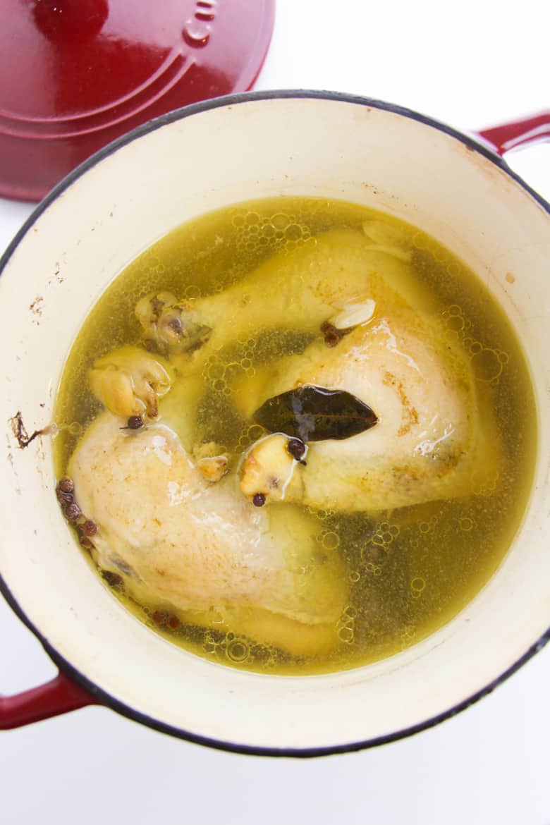 Two poached chicken leg quarters in large pot of chicken broth and seasonings