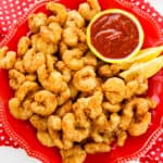 popcorn shrimp on red plate with lemon wedges and cocktail sauce
