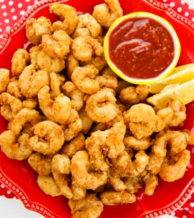 popcorn shrimp on red plate with lemon wedges and cocktail sauce