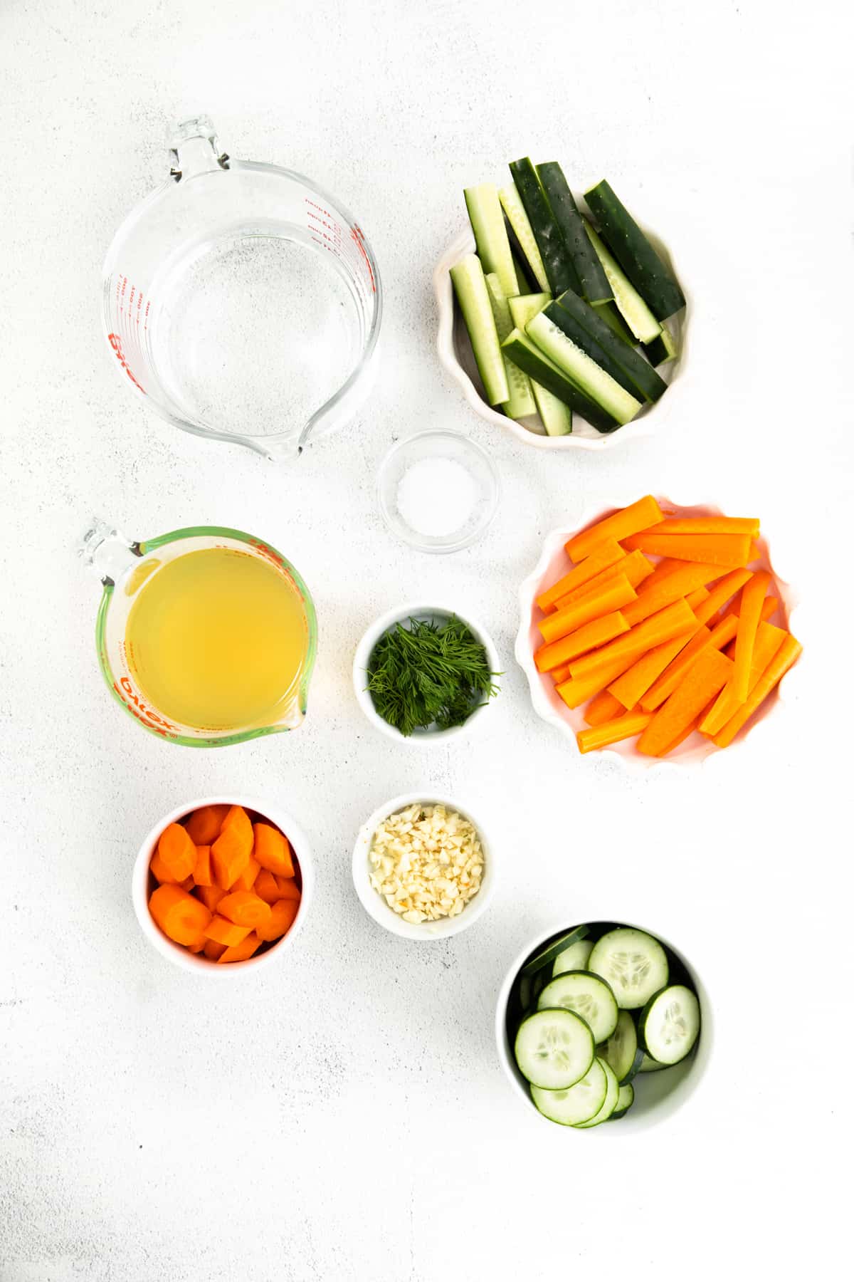 Ingredients in bowls: water, vinegar, cucumbers spears, cucumbers slices, carrot spears, carrot slices, garlic, dill, salt.
