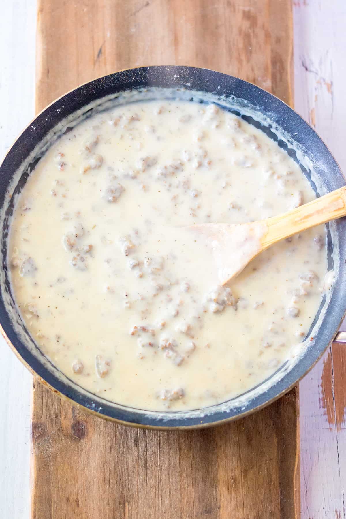 Sausage gravy in pan with wooden spoon.