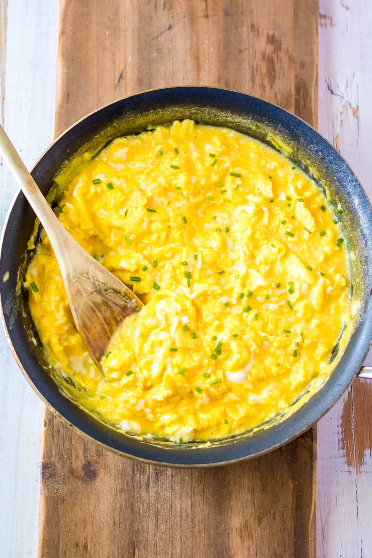 Scrambled eggs in pan with wooded spoon
