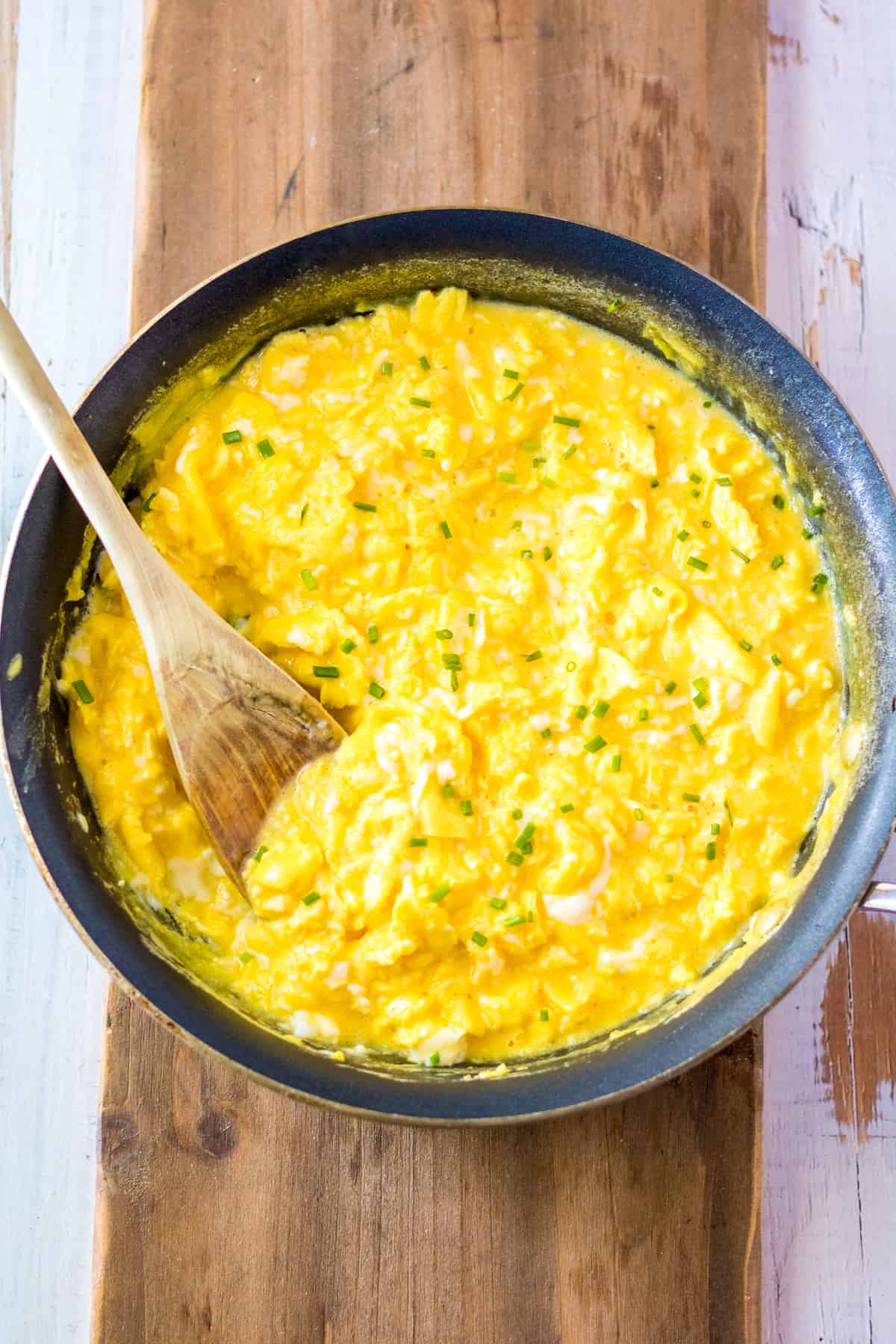 Scrambled eggs in pan with wooded spoon.