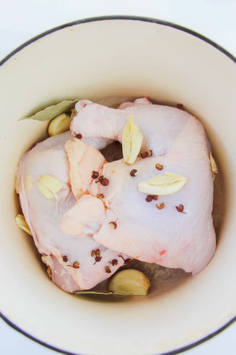 chicken quarters in large dutch oven with garlic cloves, peppercorns, and seasonings