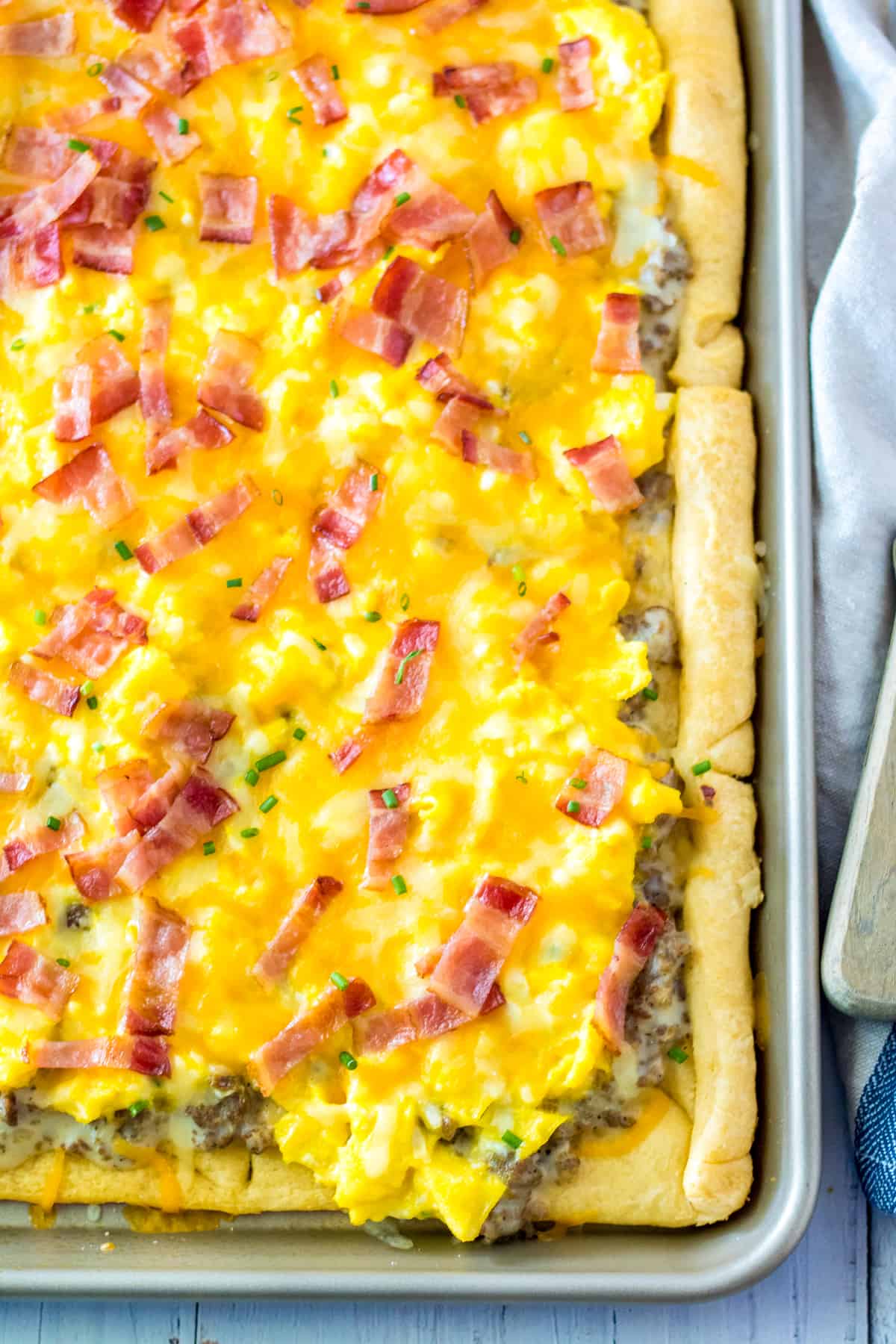 sheet pan breakfast pizza with crescent roll crust, sausage gravy sauce, scrambled eggs, cheese, and chopped bacon