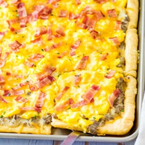 Sheet pan breakfast pizza with crescent roll crust, sausage gravy sauce, scrambled eggs, cheese, and chopped bacon.