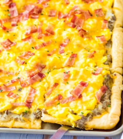 sheet pan breakfast pizza with crescent roll crust, sausage gravy sauce, scrambled eggs, cheese, and chopped bacon
