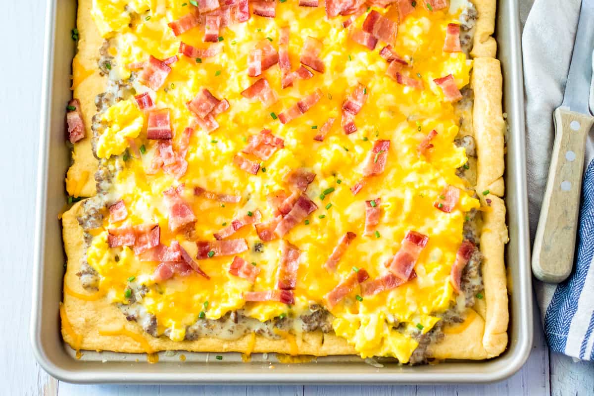 Breakfast Pizza with crescent rolls, sausage gravy, eggs, cheese, and bacon in a sheet pan.