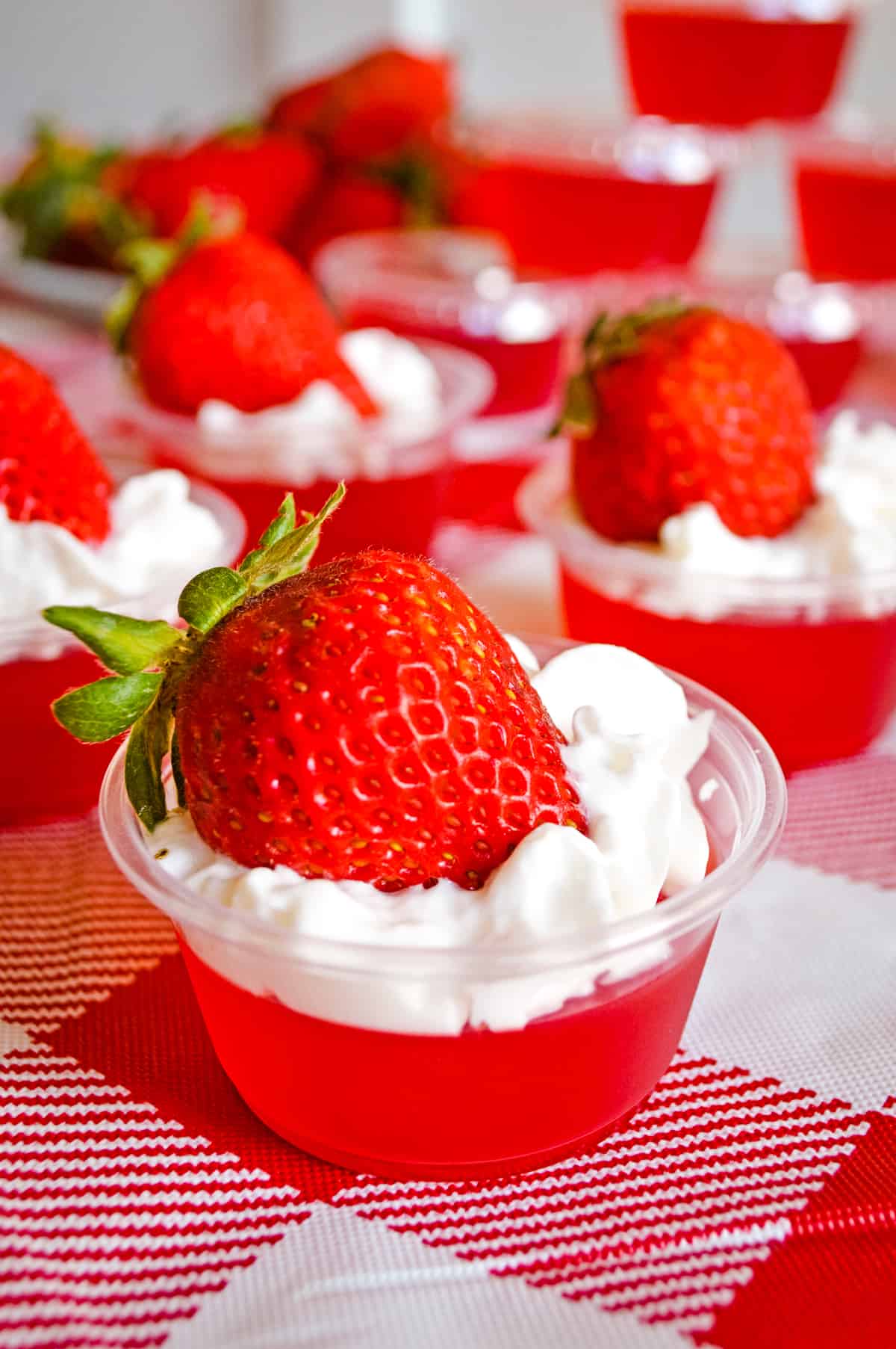 Strawberry jello shots with whipped cream and strawberry on top, served in plastic shot glasses. 