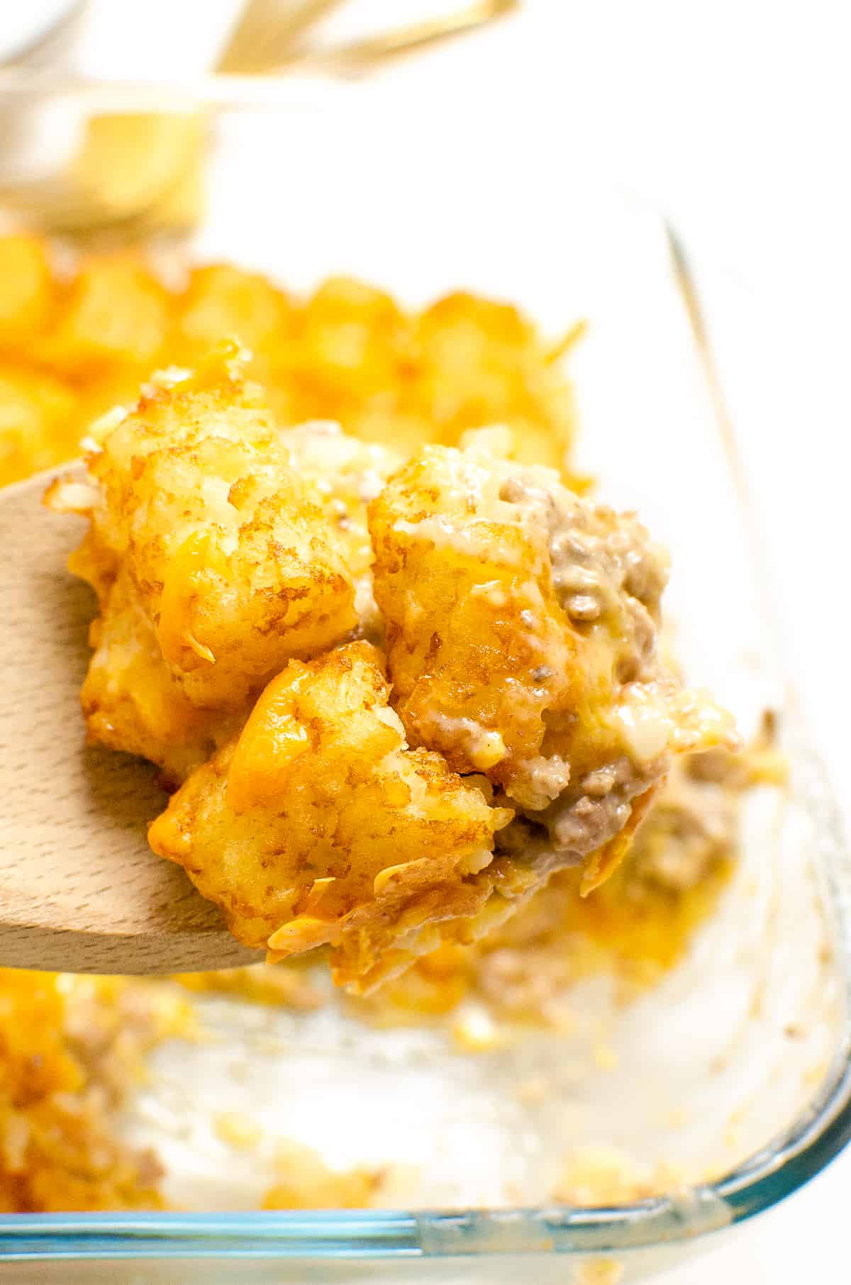 Wooden spoon full of tater tot casserole with ground beef and cheese